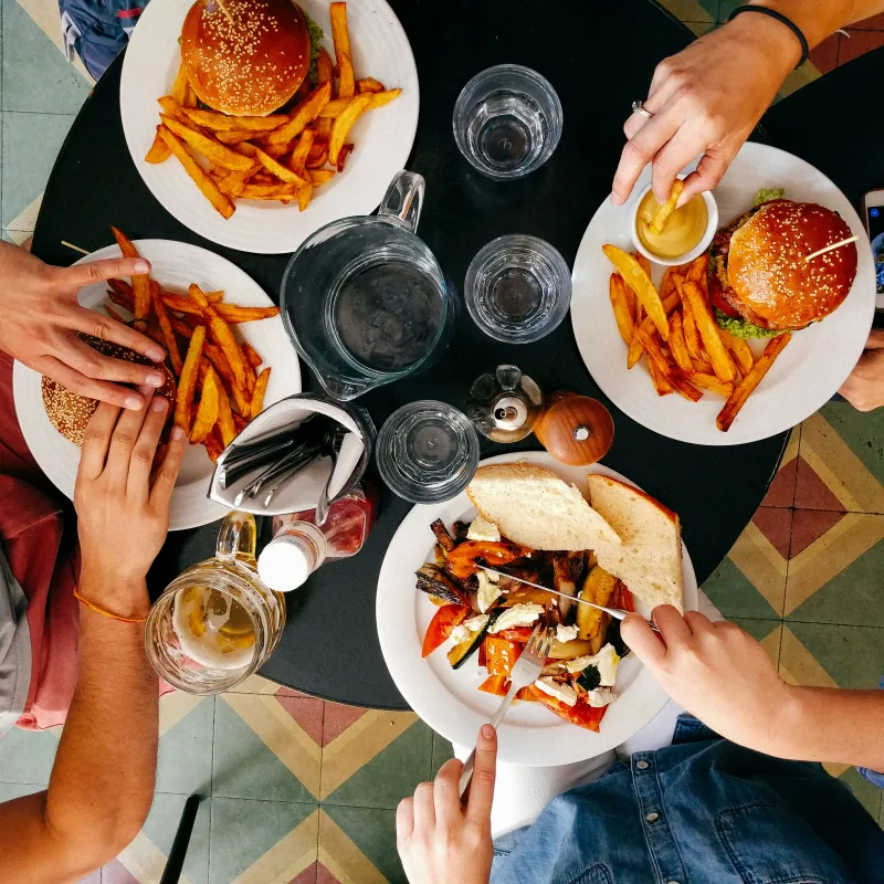 Des personnes mangeant des burgers, des frites et des légumes rôtis autour d’une table ronde, vues de dessus