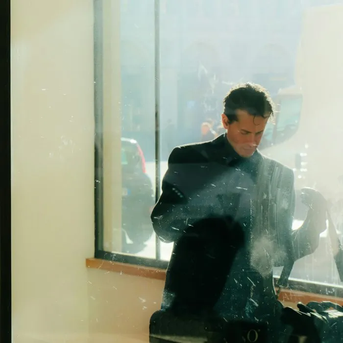 Un homme en manteau sombre derrière la fenêtre ensoleillée d’un bureau