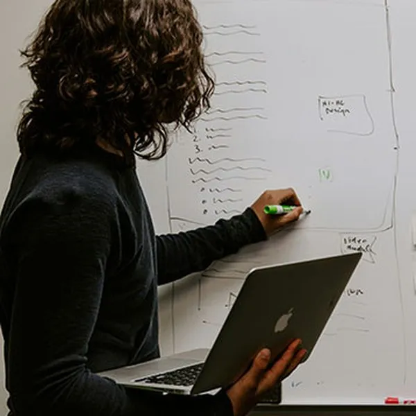 Une femme tenant un ordinateur portable prend des notes sur un tableau blanc